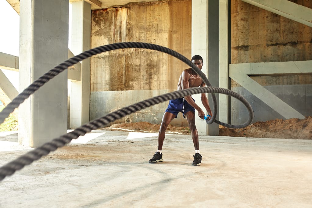 Rope workout. Sport man doing battle ropes exercise outdoor. Black male athlete exercising, doing