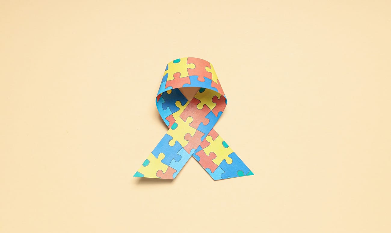 Ribbon with multi-colored puzzle pieces on a light background. World autism day concept